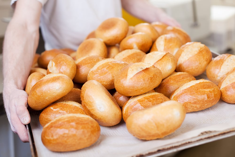 Worker holding a large tray of crispy fresh baked bread rolls in the bakery
